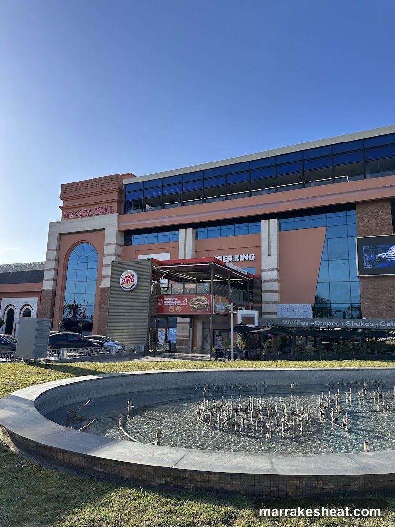 A modern Burger King storefront featuring a large glass facade and prominent signage. A circular fountain is visible in the foreground, while outdoor seating areas are partially seen to the right.