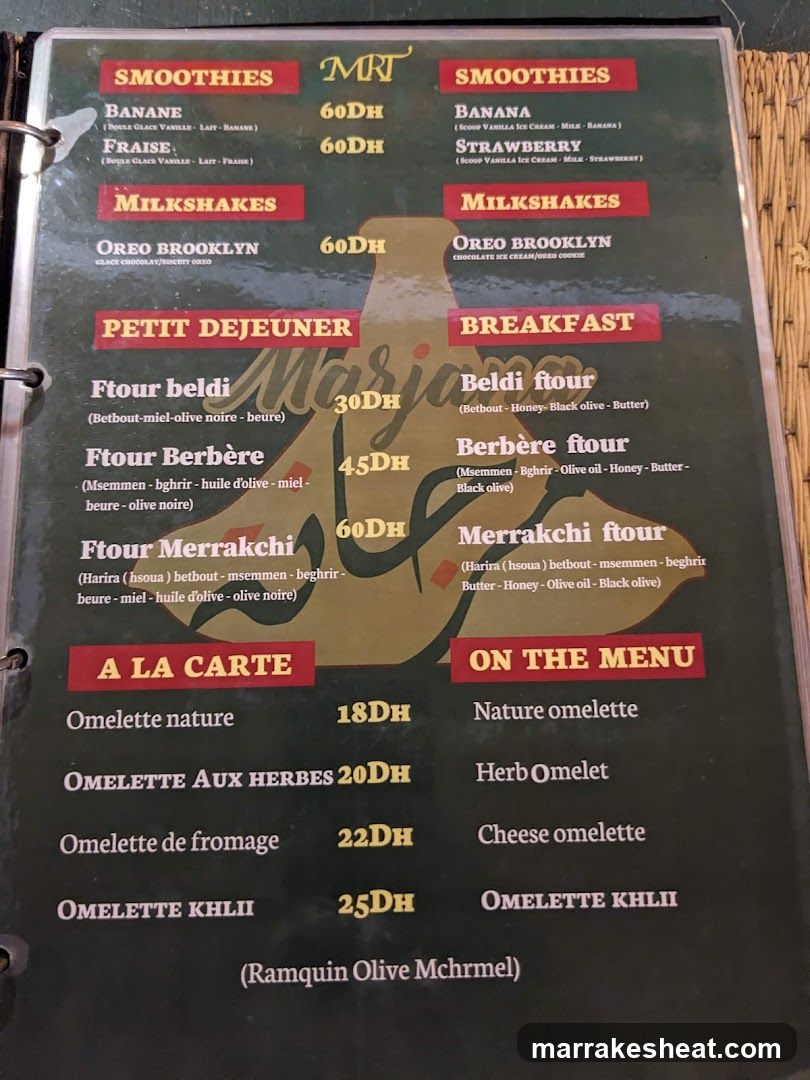 A printed menu board featuring sections like Smoothies, Milkshakes, Petit Dejeuner, Breakfast, and A La Carte with items such as Ftour beldi (30DH), Oreo Brooklyn milkshake (60DH), Nature omelette (18DH), Herb Omelet (20DH), Cheese omelette (22DH), and Omelette Khlii (25DH). The menu is bilingual in French and English.
