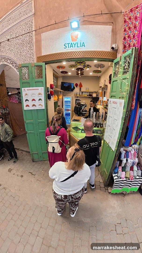 A group of people standing in front of a coffee shop entrance with green doors and colorful interior decor, including hanging lights and shelves displaying products.